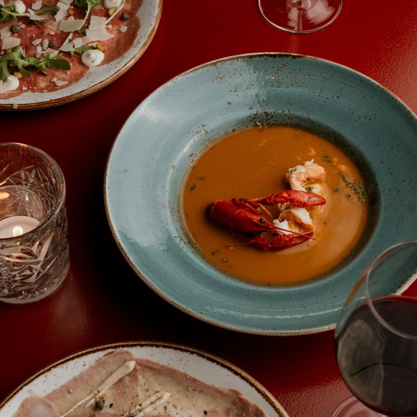 Bisque and small plates on a red table at Mej Janssen